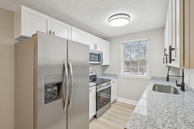 kitchen featuring baseboards, light wood-style flooring, light stone countertops, stainless steel appliances, and white cabinetry