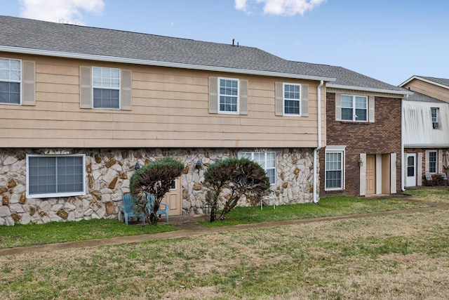 view of front of property featuring stone siding, a shingled roof, a front yard, and brick siding