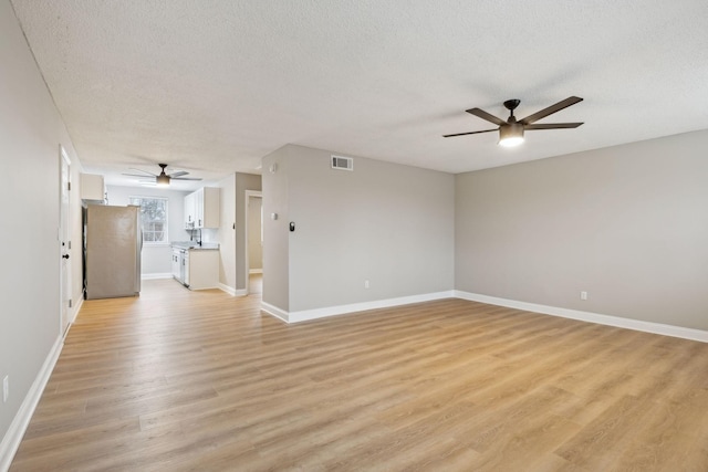 empty room featuring baseboards, visible vents, light wood-style flooring, and a textured ceiling