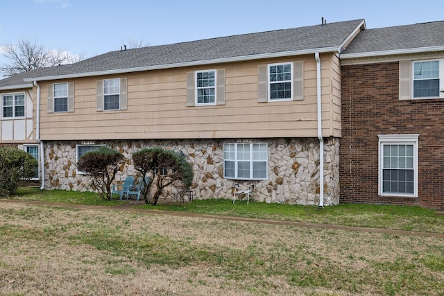 rear view of house with stone siding, a yard, and a shingled roof