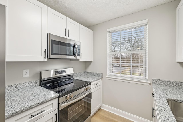 kitchen featuring white cabinetry, a textured ceiling, appliances with stainless steel finishes, and baseboards