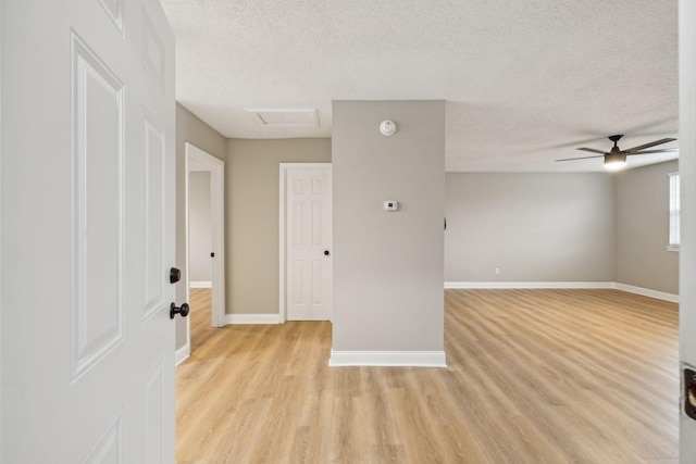 empty room with light wood-style floors, attic access, ceiling fan, a textured ceiling, and baseboards