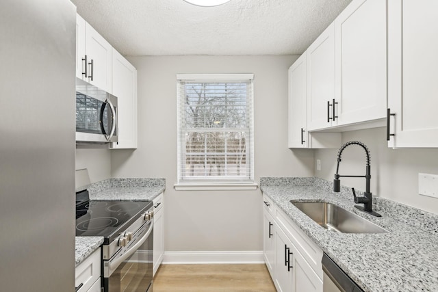 kitchen with baseboards, light wood-style flooring, stainless steel appliances, white cabinetry, and a sink