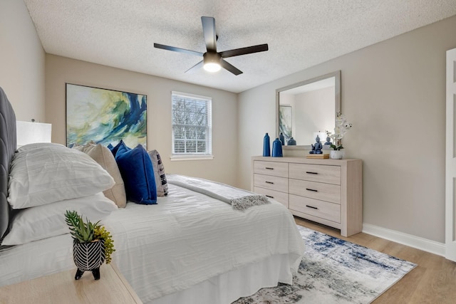 bedroom with a textured ceiling, ceiling fan, light wood-style flooring, and baseboards