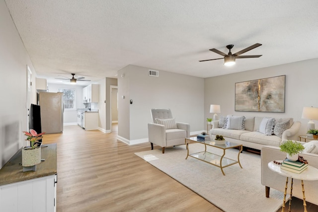 living room with visible vents, light wood-style flooring, ceiling fan, a textured ceiling, and baseboards