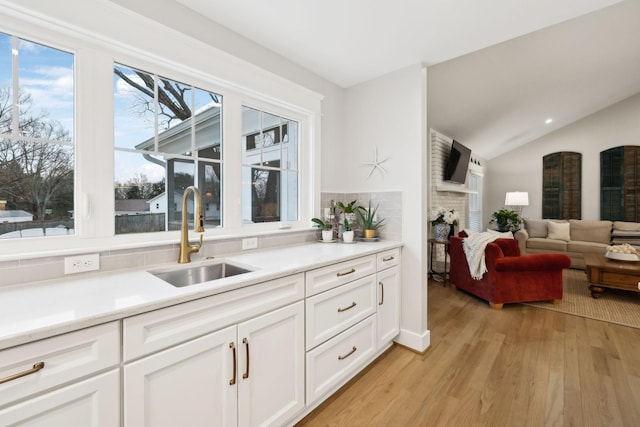 kitchen with light wood-style flooring, a fireplace, a sink, vaulted ceiling, and decorative backsplash