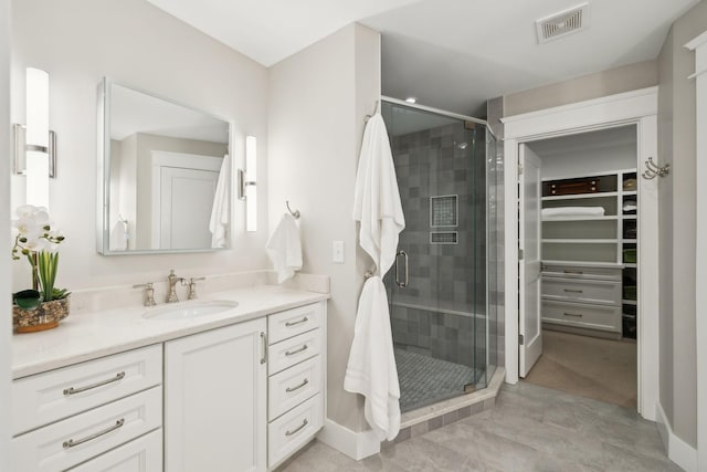 full bath featuring vanity, a shower stall, visible vents, and a walk in closet