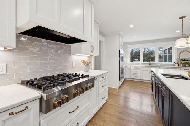 kitchen with appliances with stainless steel finishes, custom range hood, white cabinetry, and a sink