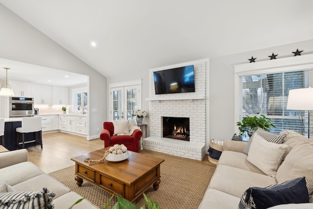 living room featuring high vaulted ceiling, recessed lighting, a fireplace, french doors, and light wood finished floors