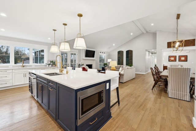 kitchen with stainless steel microwave, light countertops, light wood-type flooring, white cabinetry, and a sink