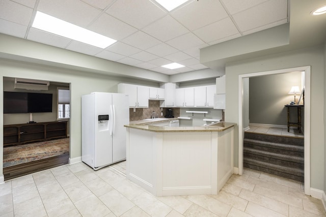 kitchen featuring a paneled ceiling, a peninsula, white refrigerator with ice dispenser, white cabinetry, and decorative backsplash