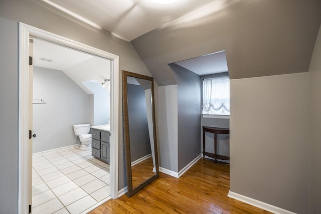 bathroom with baseboards, toilet, wood finished floors, vaulted ceiling, and vanity