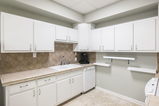 kitchen with white dishwasher, a sink, white cabinetry, light countertops, and decorative backsplash