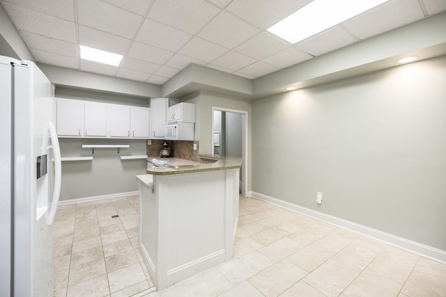 kitchen featuring a peninsula, white appliances, baseboards, and a drop ceiling