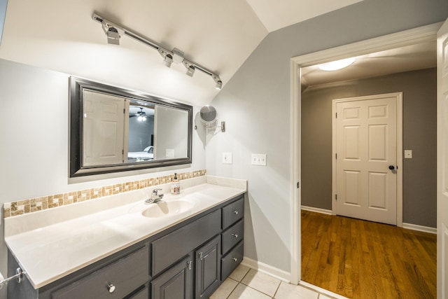 bathroom with vanity, baseboards, vaulted ceiling, decorative backsplash, and tile patterned floors