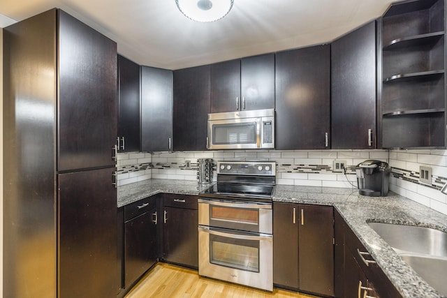 kitchen featuring open shelves, light wood-style flooring, decorative backsplash, appliances with stainless steel finishes, and a sink