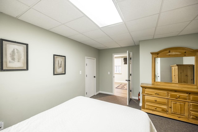 bedroom with a drop ceiling, dark carpet, and baseboards