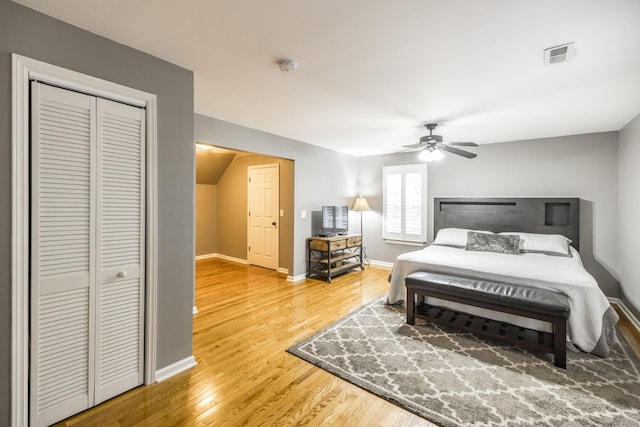 bedroom with wood finished floors, a ceiling fan, visible vents, baseboards, and a closet