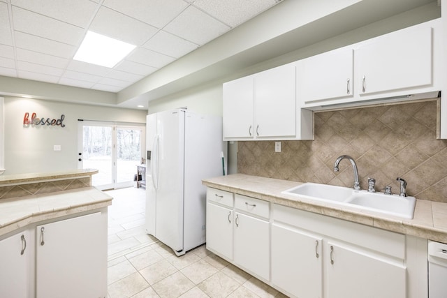 kitchen featuring white cabinets, a sink, light countertops, white fridge with ice dispenser, and backsplash