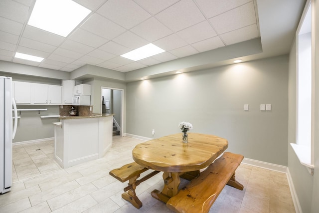 kitchen with a paneled ceiling, white appliances, white cabinets, and baseboards