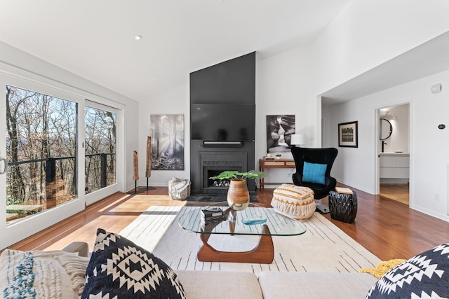 living area with lofted ceiling, a large fireplace, baseboards, and wood finished floors