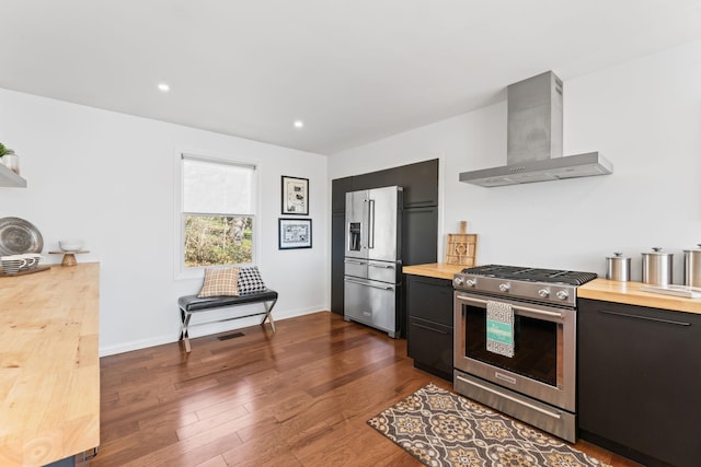 kitchen featuring wall chimney exhaust hood, appliances with stainless steel finishes, dark wood-style flooring, and wood counters