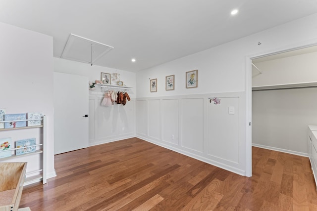 empty room with recessed lighting, a decorative wall, attic access, wainscoting, and wood finished floors