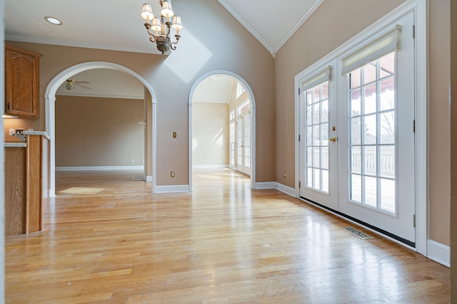 unfurnished room featuring arched walkways, light wood-style flooring, baseboards, french doors, and ornamental molding