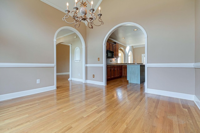 empty room with ornamental molding, arched walkways, and light wood-style flooring