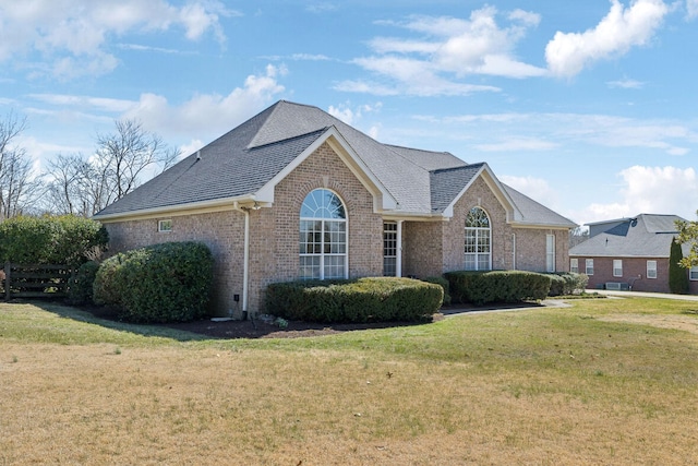 view of front of home with a shingled roof, a front yard, and brick siding