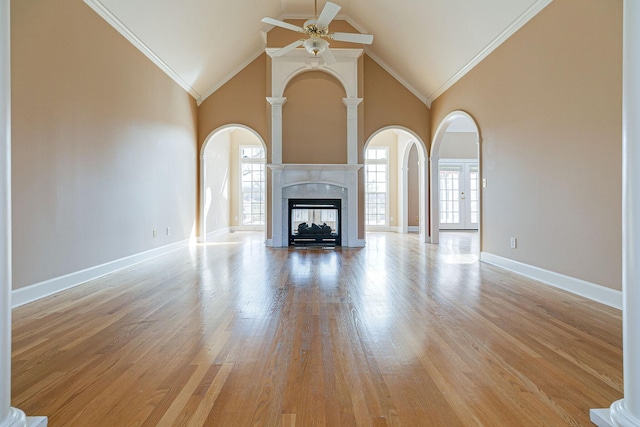 unfurnished living room with light wood finished floors, baseboards, arched walkways, ceiling fan, and crown molding