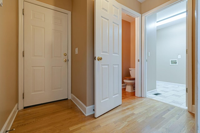 hall with light wood-type flooring, visible vents, and baseboards