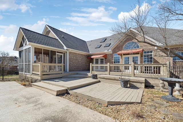 rear view of property with roof with shingles, brick siding, a sunroom, fence, and a wooden deck