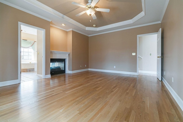 unfurnished living room with baseboards, a tray ceiling, crown molding, light wood-type flooring, and a multi sided fireplace