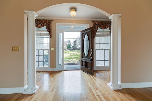 foyer featuring arched walkways, wood finished floors, baseboards, ornate columns, and crown molding