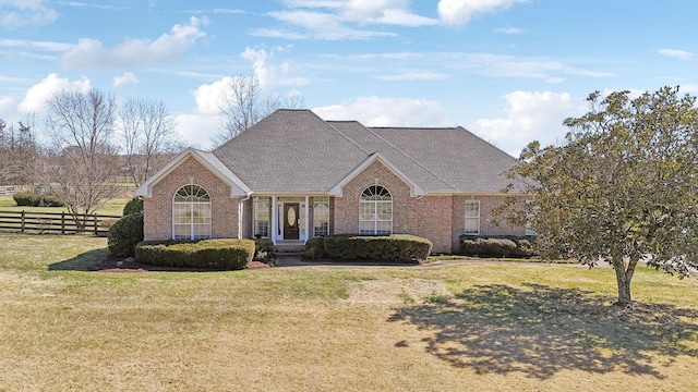 view of front of house with brick siding, a front lawn, a shingled roof, and fence