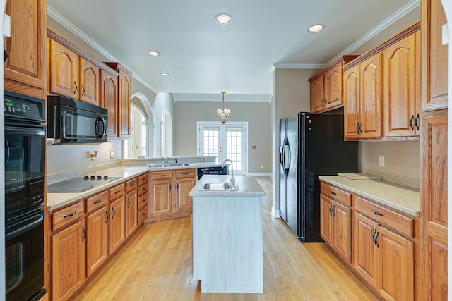 kitchen featuring a kitchen island with sink, a peninsula, a sink, light countertops, and black appliances