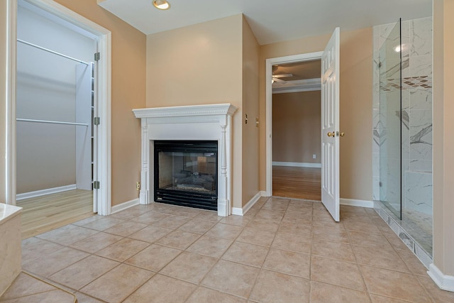 unfurnished living room featuring a glass covered fireplace, light tile patterned flooring, ceiling fan, and baseboards