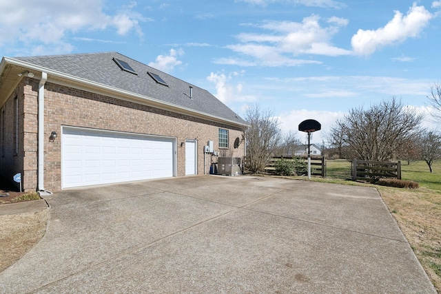 view of side of property featuring driveway, a shingled roof, central AC unit, fence, and brick siding