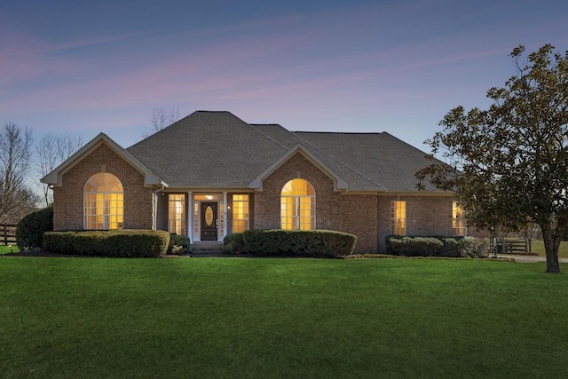 ranch-style home featuring a shingled roof, a lawn, and brick siding