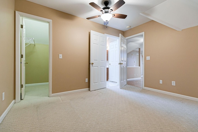 unfurnished bedroom with a walk in closet, a closet, a ceiling fan, light carpet, and baseboards