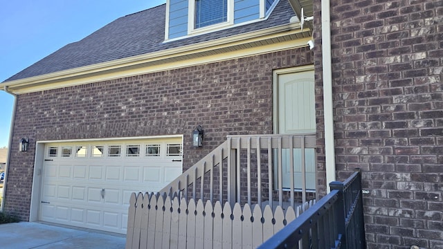 exterior space featuring a garage, concrete driveway, brick siding, and a shingled roof