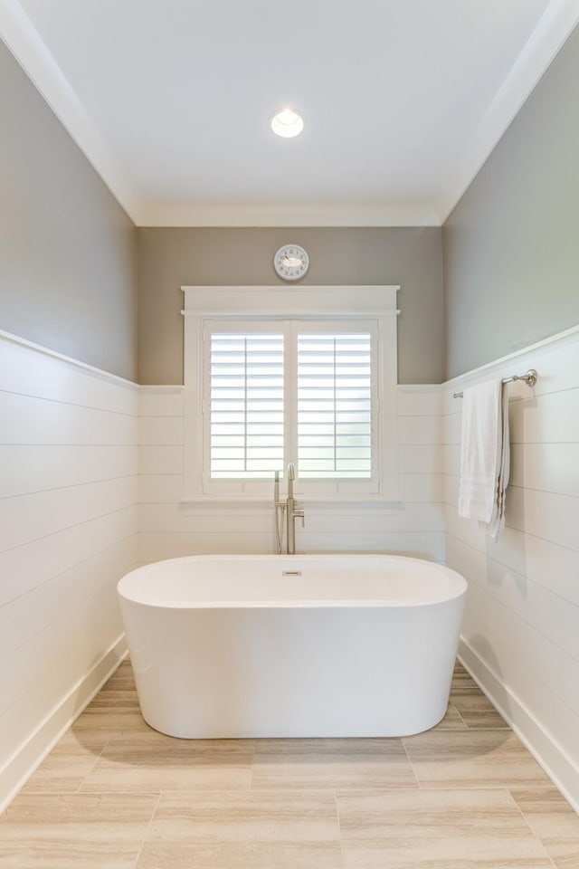 full bath with crown molding, wainscoting, a freestanding bath, and tile walls