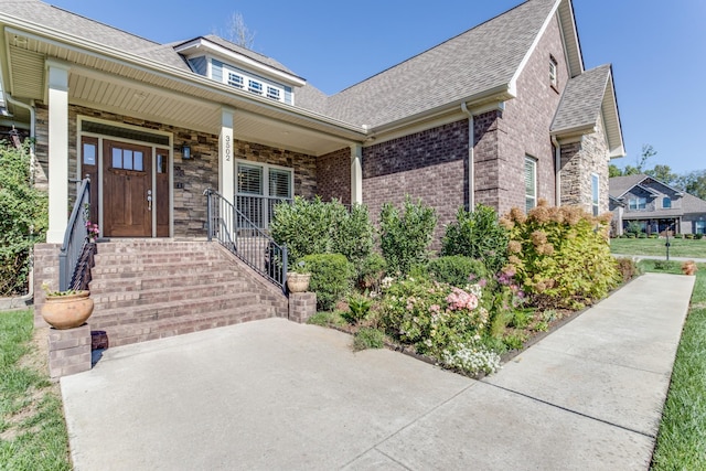 view of front of house featuring covered porch, brick siding, and roof with shingles