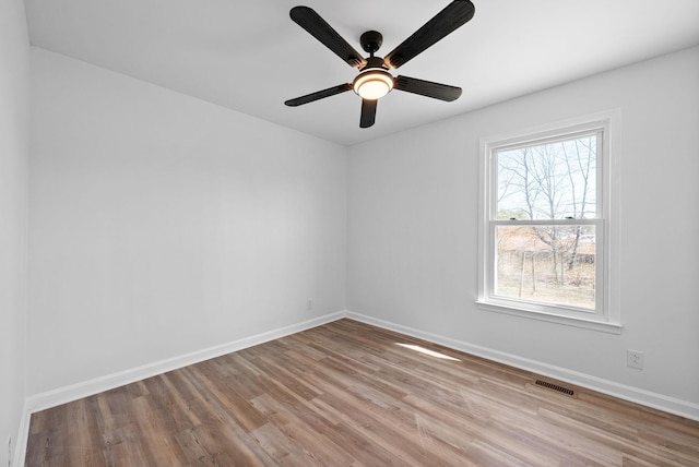 empty room with a ceiling fan, wood finished floors, visible vents, and baseboards