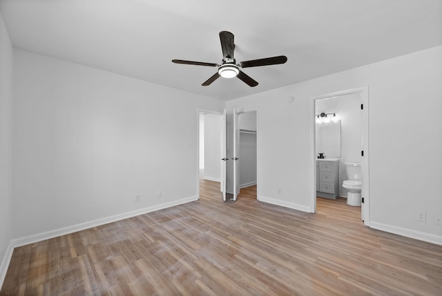 unfurnished bedroom featuring connected bathroom, baseboards, a closet, light wood finished floors, and a walk in closet