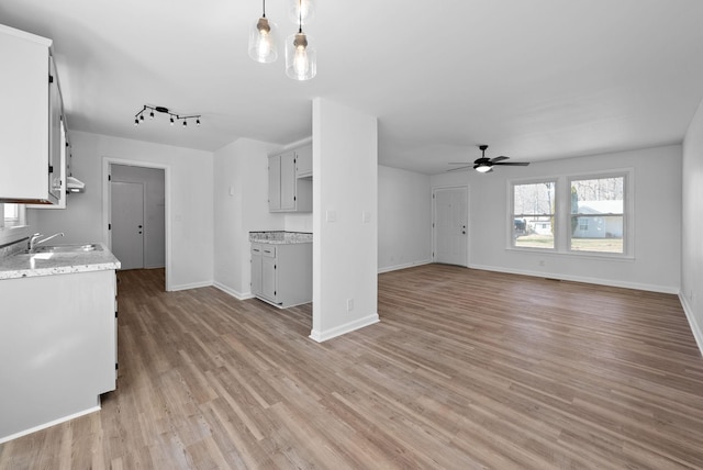 kitchen with decorative light fixtures, light wood-style flooring, a ceiling fan, a sink, and baseboards