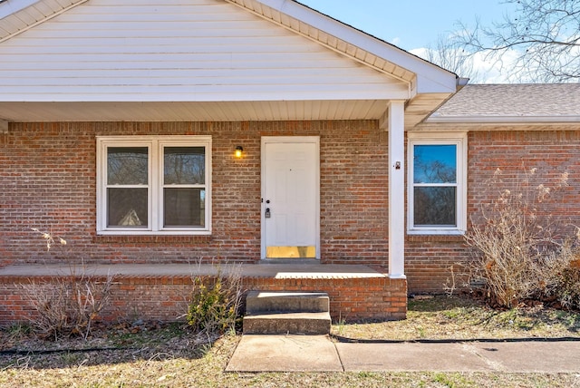 view of exterior entry featuring roof with shingles and brick siding