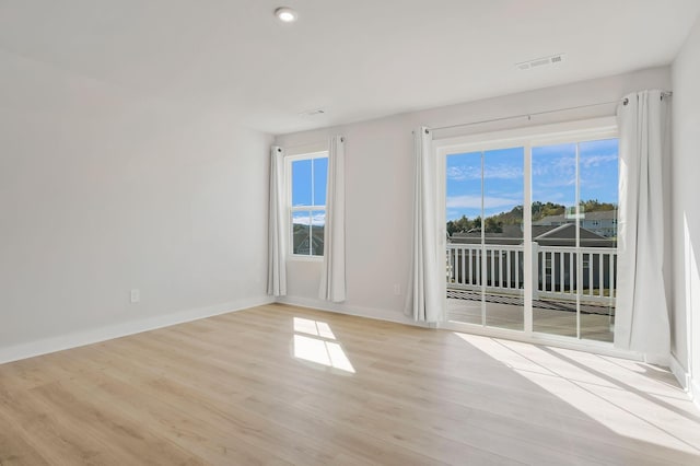 spare room featuring light wood finished floors, plenty of natural light, visible vents, and baseboards