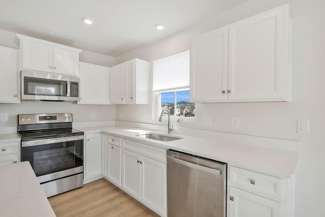 kitchen with light countertops, appliances with stainless steel finishes, white cabinetry, a sink, and light wood-type flooring